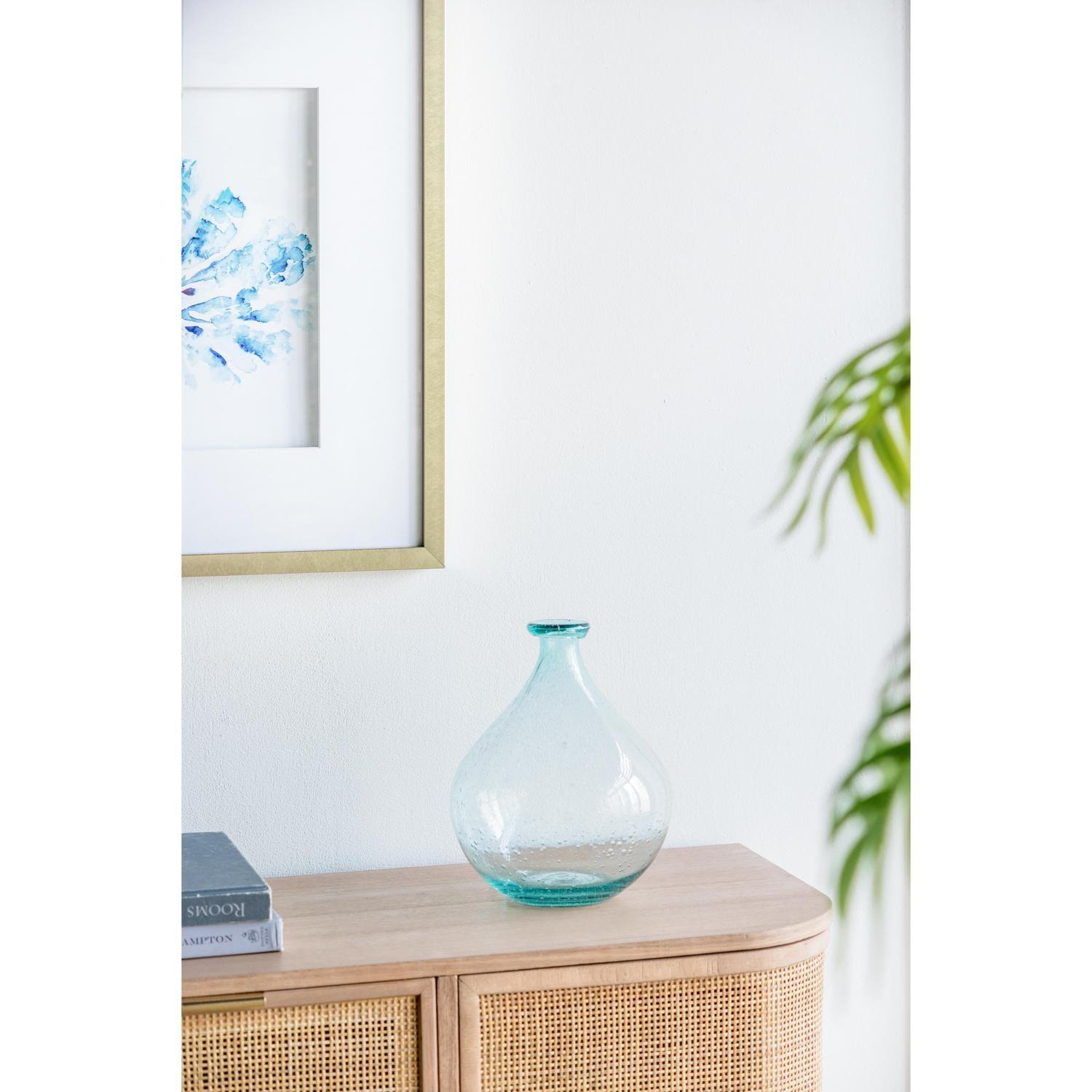 Blue glass vase on wood cabinet in front of blue picture