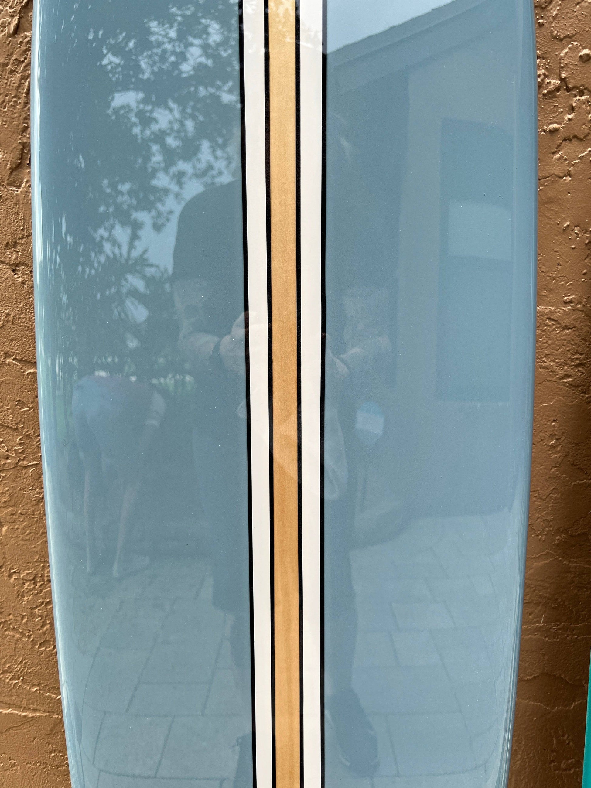 A light blue surfboard featuring three vertical stripes in gold and black.