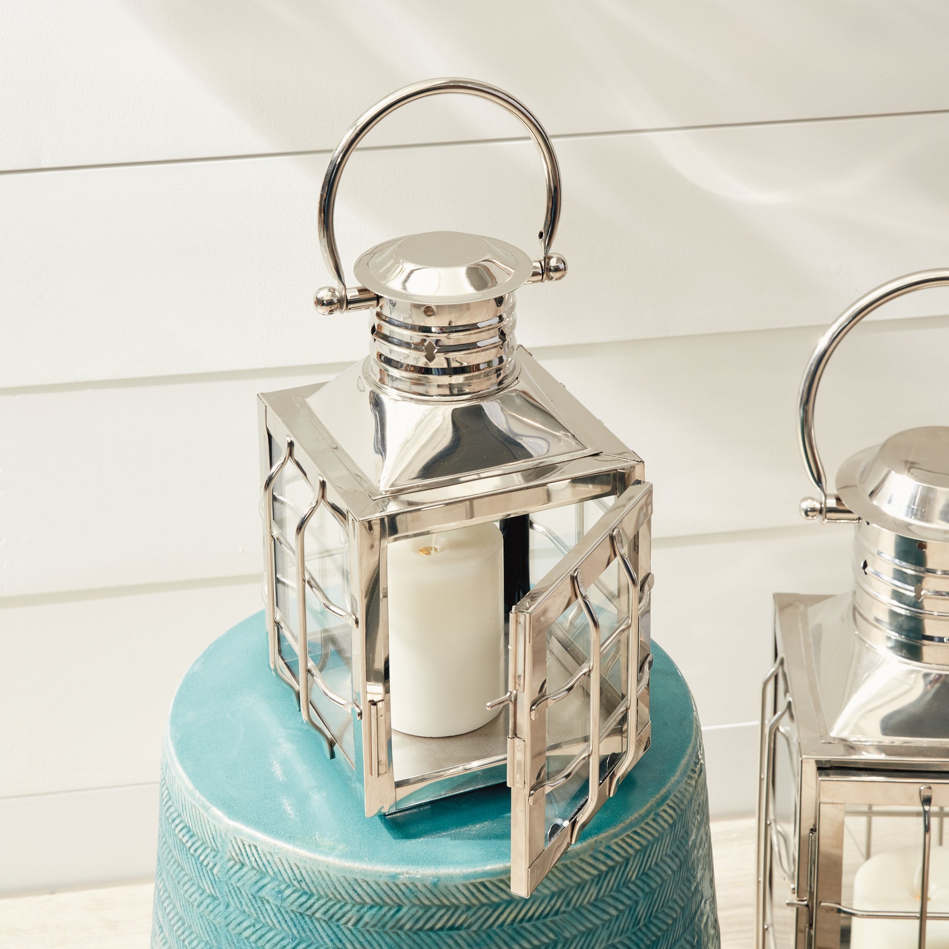 Silver lantern with open door displaying a white candle, set on a textured turquoise table.