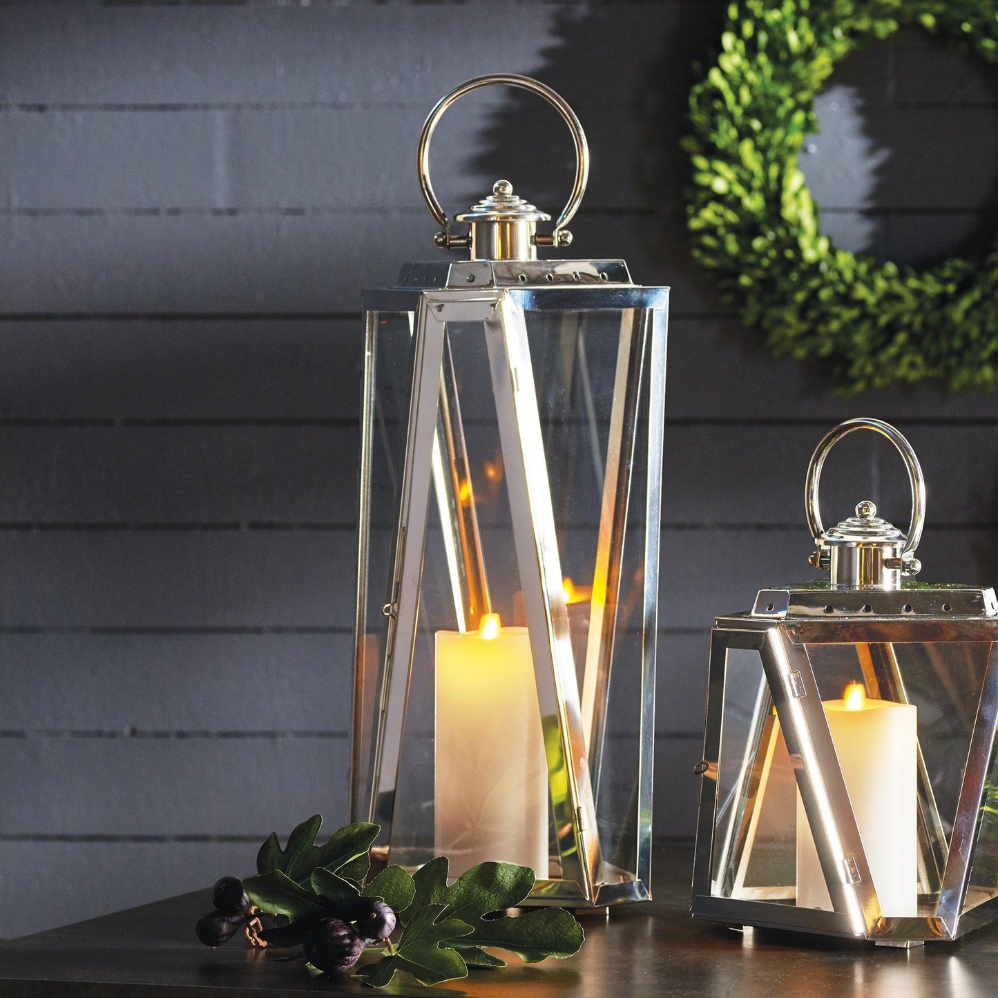 Two silver lanterns with candles on a table with wreaths