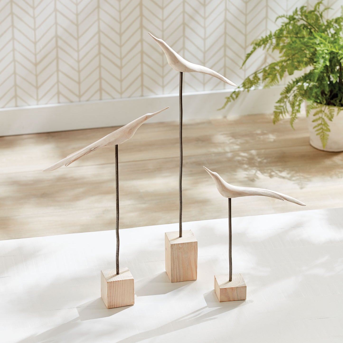 three white wooden birds on stands on white floor