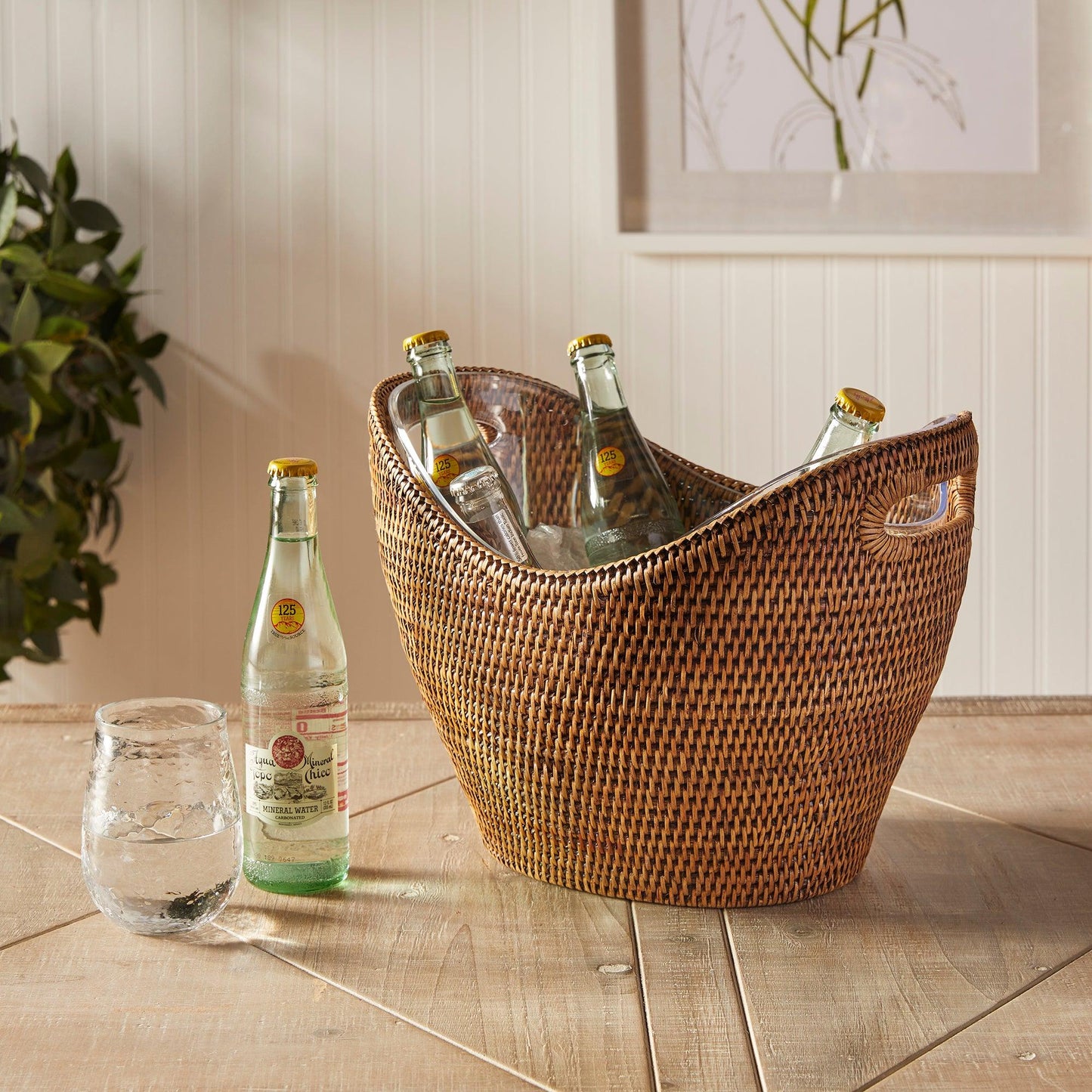 a wicker basket filled with bottles of beer next to a glass
