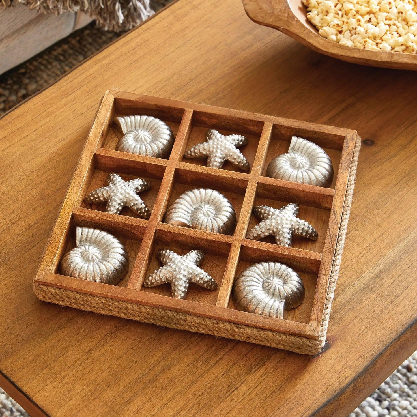 Wood tic tac toe board with silver pieces on a wood table