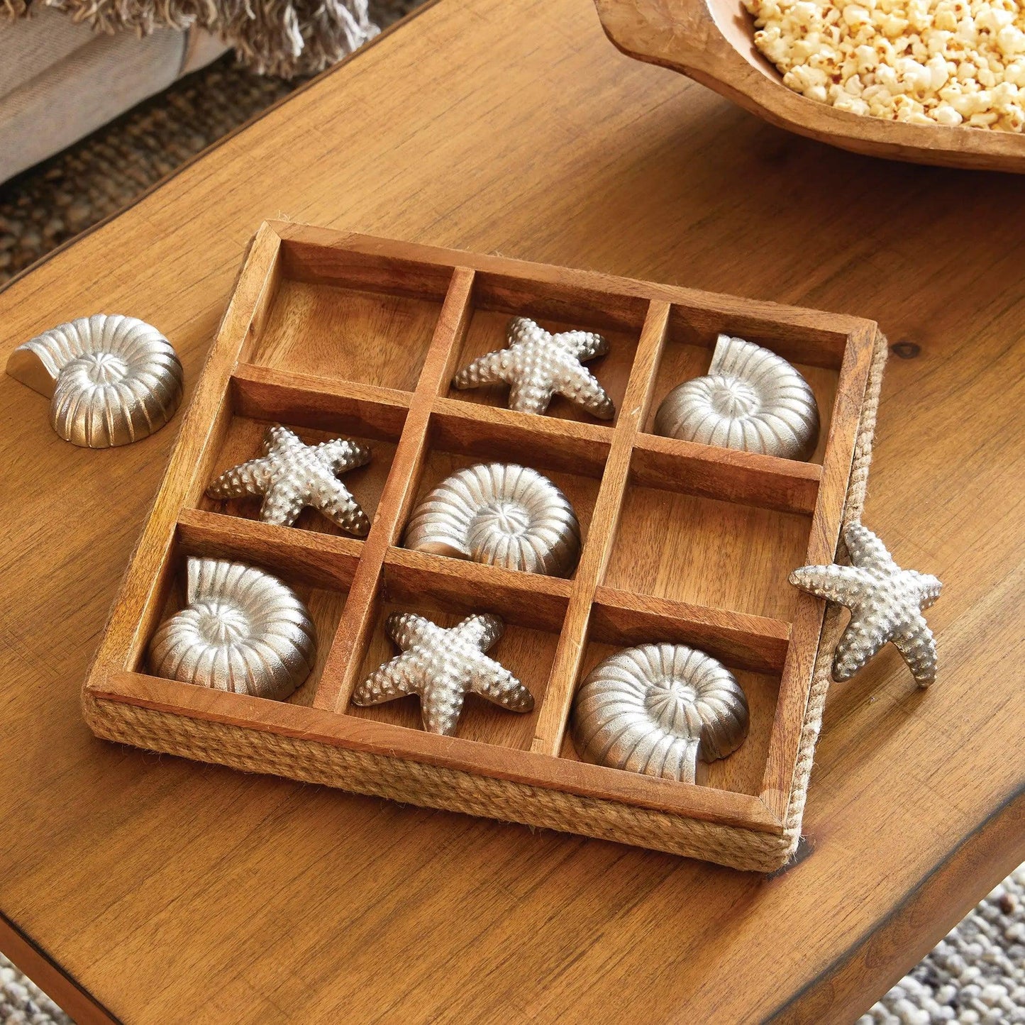 Wood tic tac toe board with silver pieces on a wood table.