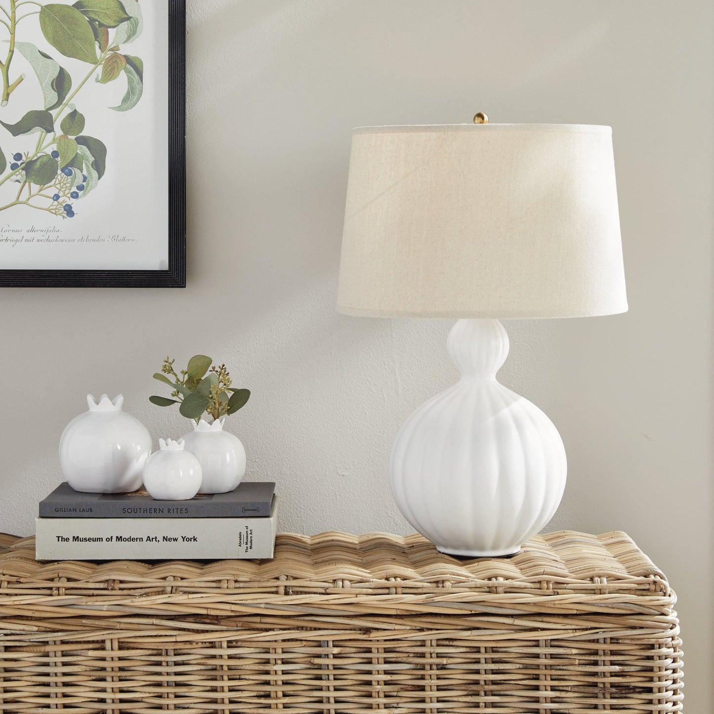 white lamp on a wicker table next to books and white vases