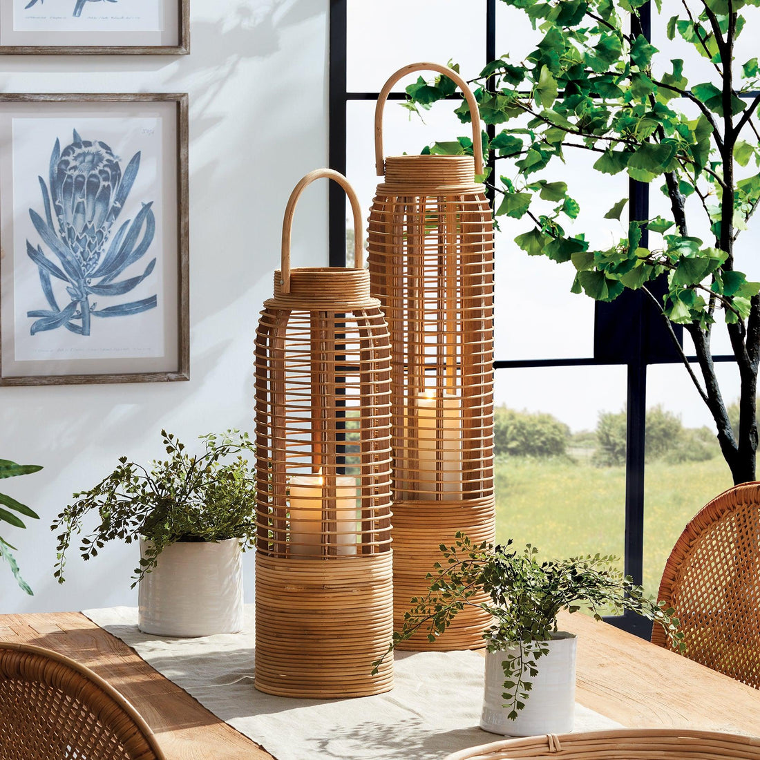 Pair of rattan lanterns styled on a dining table with coastal wall art and greenery