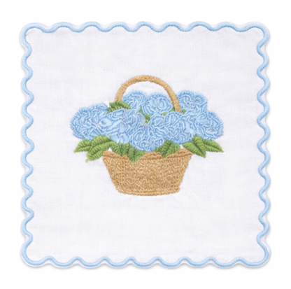 White cocktail napkin embroidered with blue hydrangeas in a tan basket, green leaves, and a light blue scalloped border
