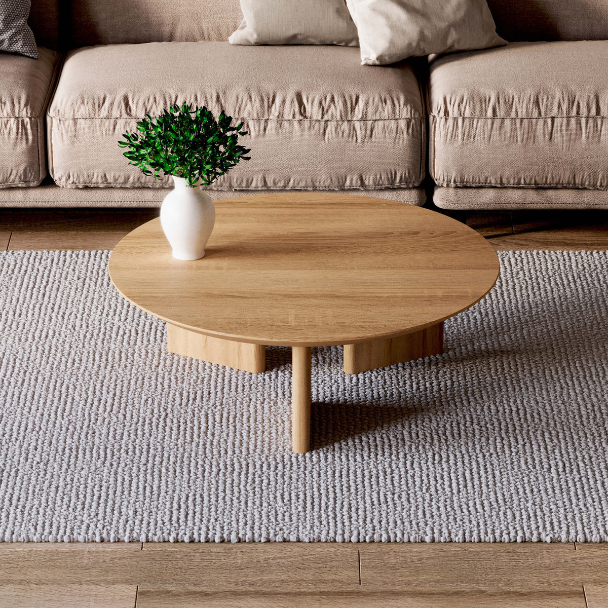 Elevated view of the Noah round coffee table showing oak grain and a white vase