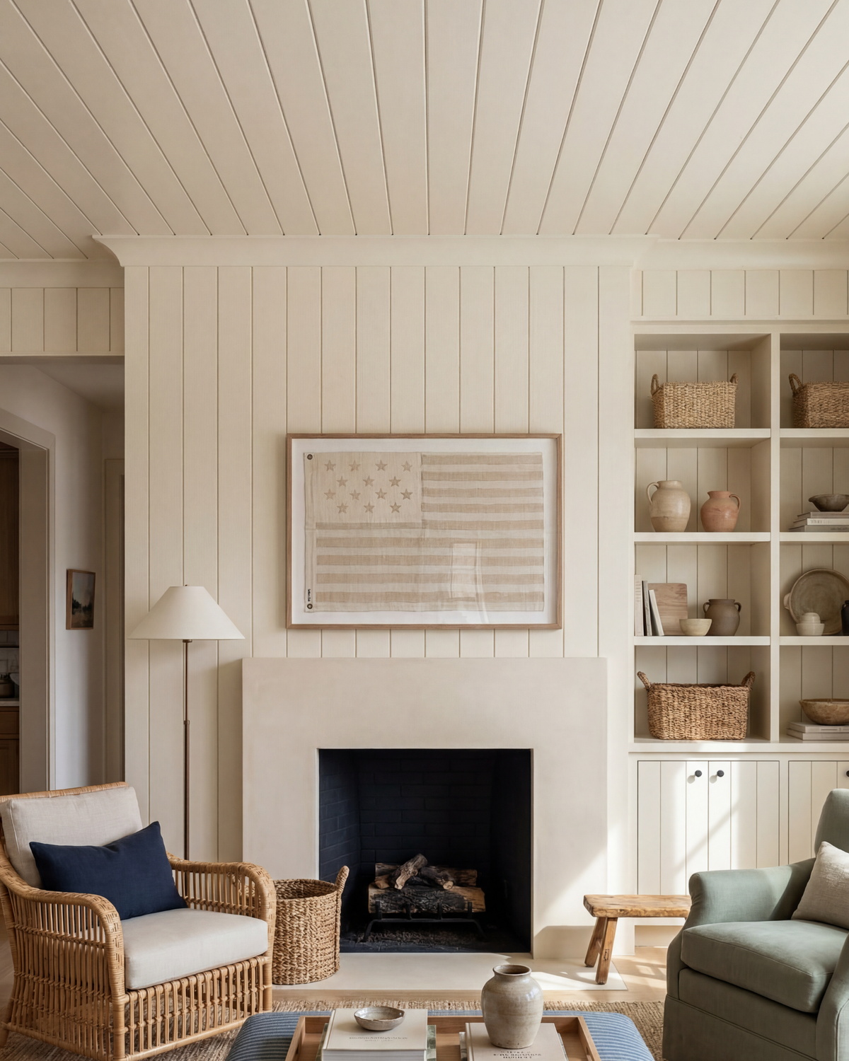 Framed sand-toned American flag above a fireplace in a white paneled living room with woven seating.