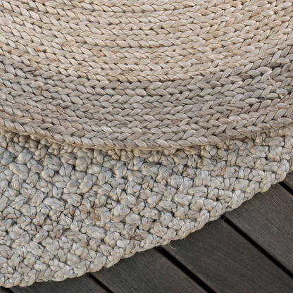 Natural jute rug styled beneath a sculptural wooden side table beside a woven chair