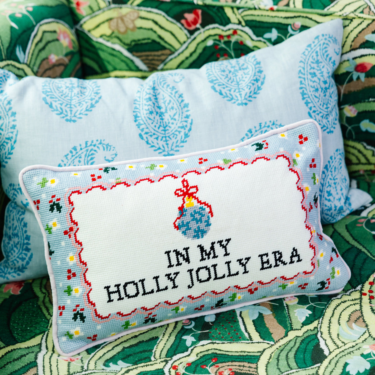 Holly Jolly Era pillow layered with a blue patterned cushion on a green upholstered chair