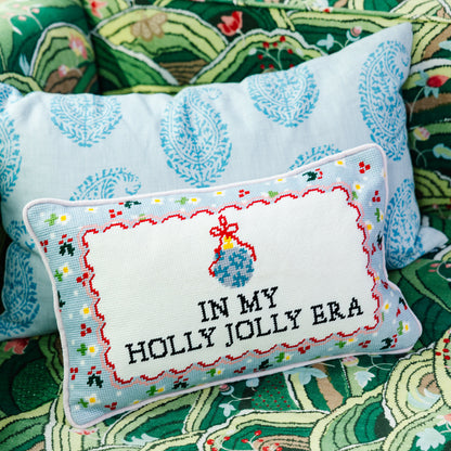 Holly Jolly Era pillow layered with a blue patterned cushion on a green upholstered chair