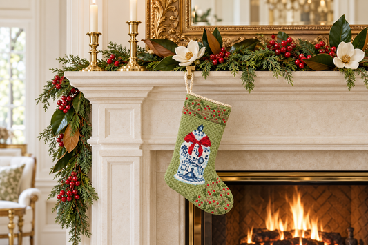 Green ginger jar needlepoint Christmas stocking with a red bow hanging from a mantel decorated with holiday greenery