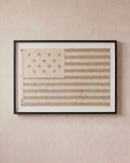 Sand-toned embroidered American flag displayed horizontally in a black shadowbox frame.