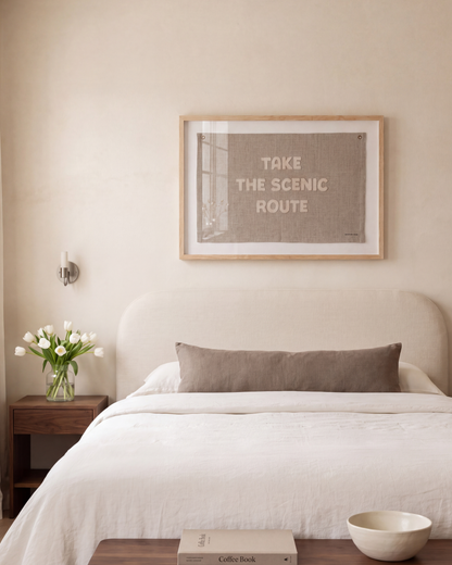 Scenic Route framed flag hanging above a neutral upholstered bed