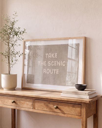 Wood-framed Scenic Route flag styled on a console with a potted tree and stacked books