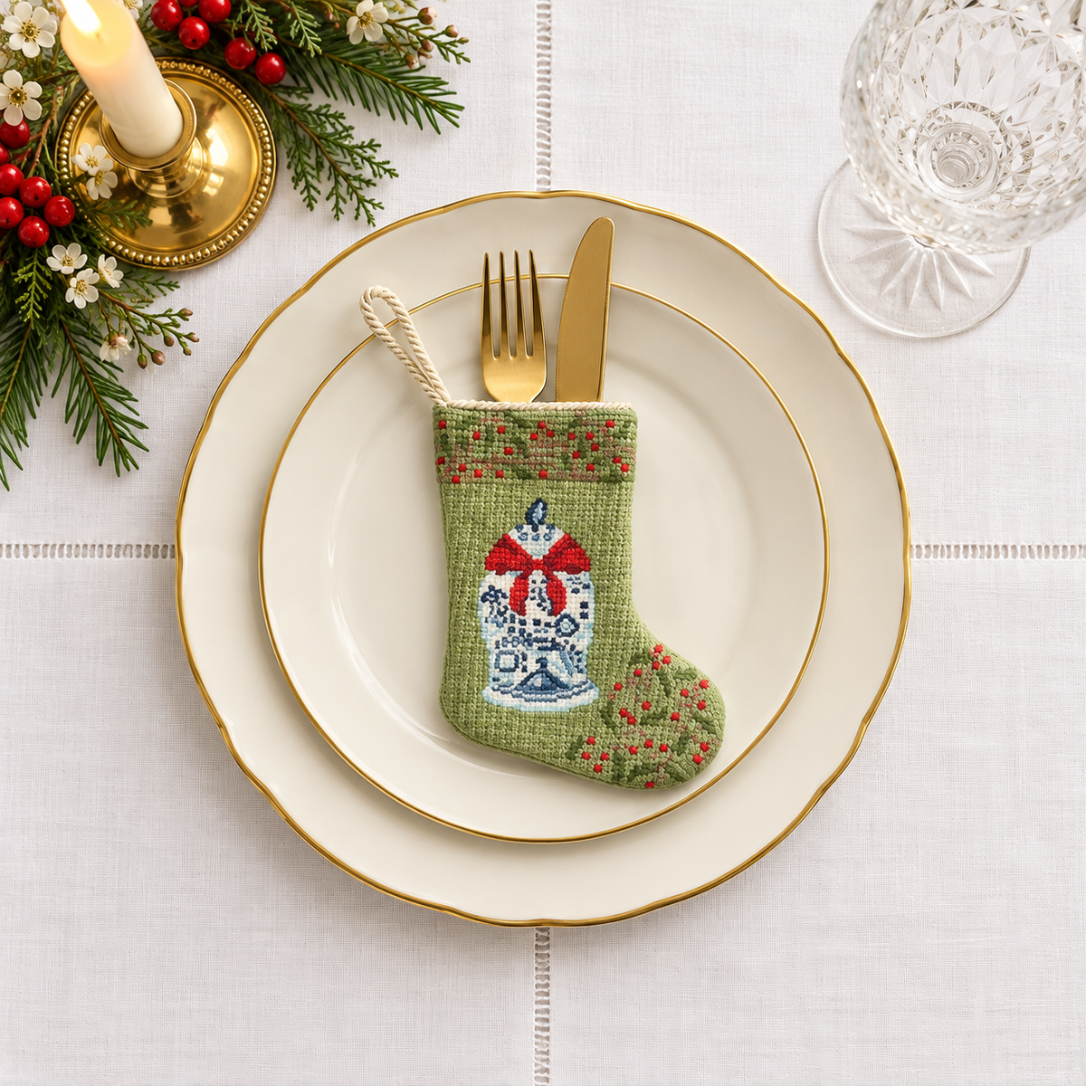 Mini ginger jar needlepoint stocking holding gold-colored flatware on a white holiday place setting