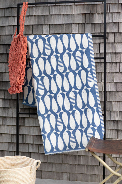 LUCA Sardines throw blanket hanging against a shingled wall beside a coral-colored net bag