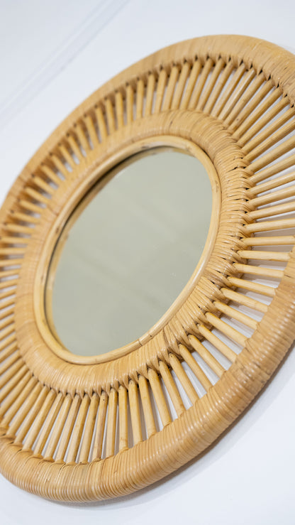 Angled view of the round rattan mirror showing its wrapped borders and radiating cane details
