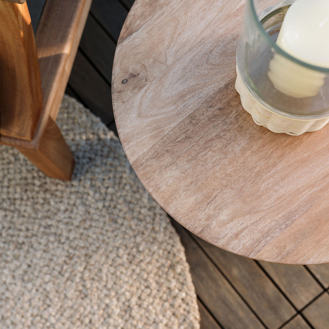 Detail of a natural jute rug beneath a round wooden side table beside an armchair