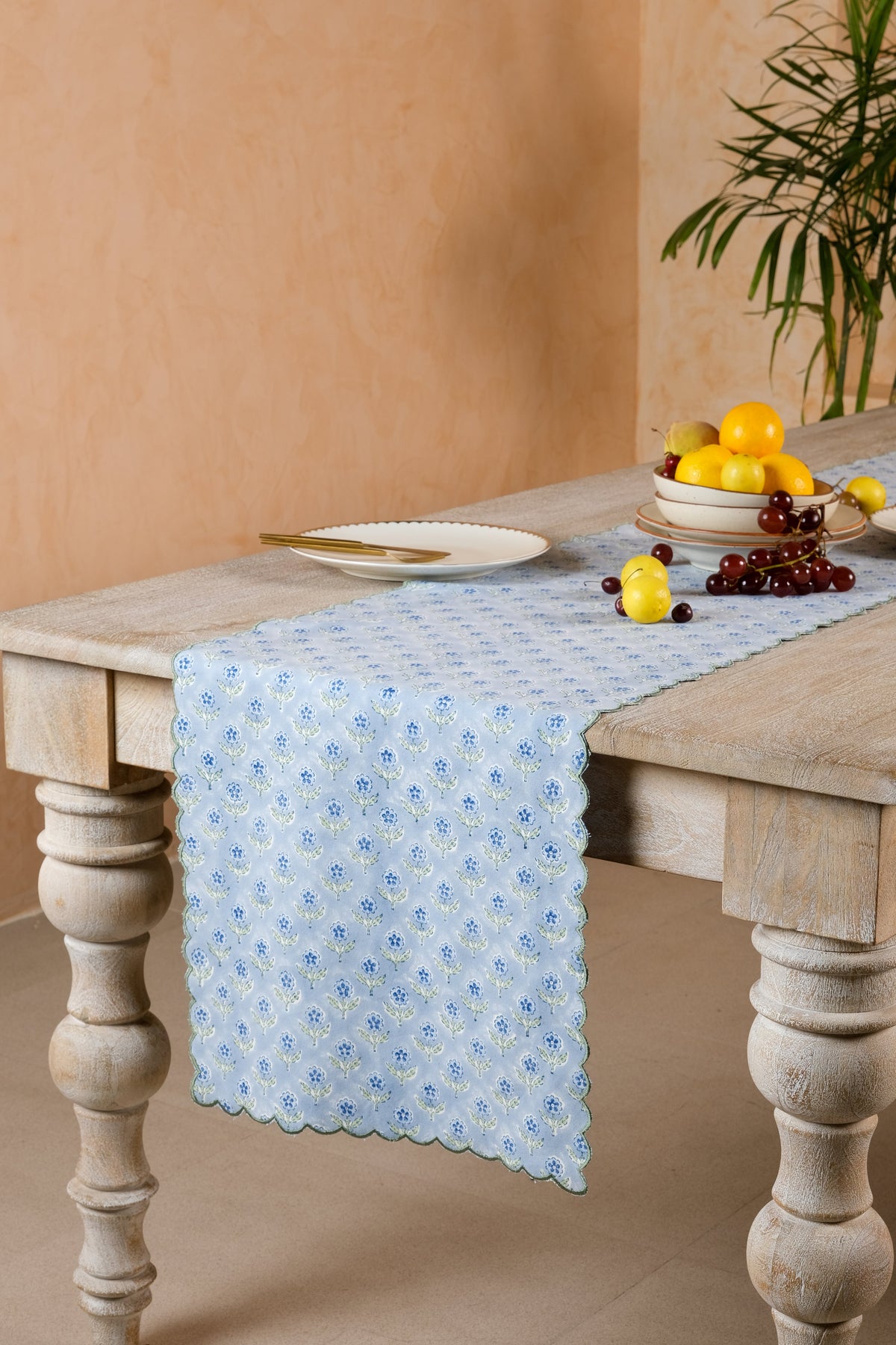 Blue floral blockprint table runner extending along a wood dining table, showing its scalloped end and green embroidered border.