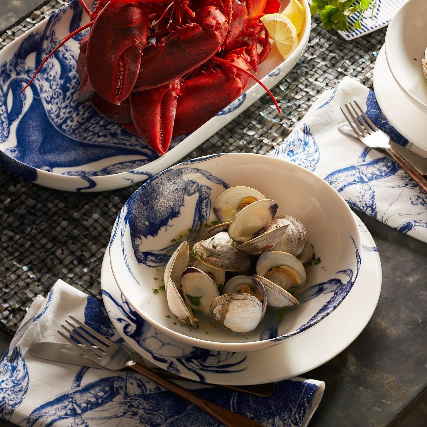 a bowl of clams sits on a table next to a plate of lobsters