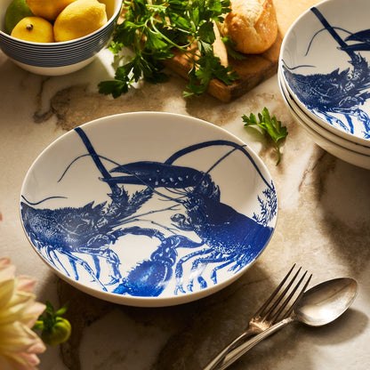	Blue Lobster Entrée Bowl on a kitchen counter beside lemons, herbs, bread, and stacked matching bowls