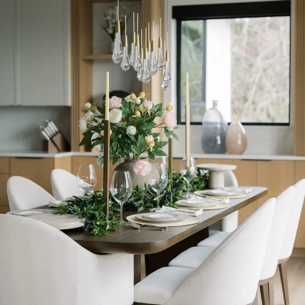 Gold-finish iron taper candle holders arranged along a dining table with greenery and white chairs