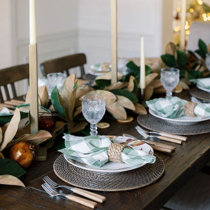 Gold-finish square iron candle holders with ivory taper candles on a dining table with green and white place settings