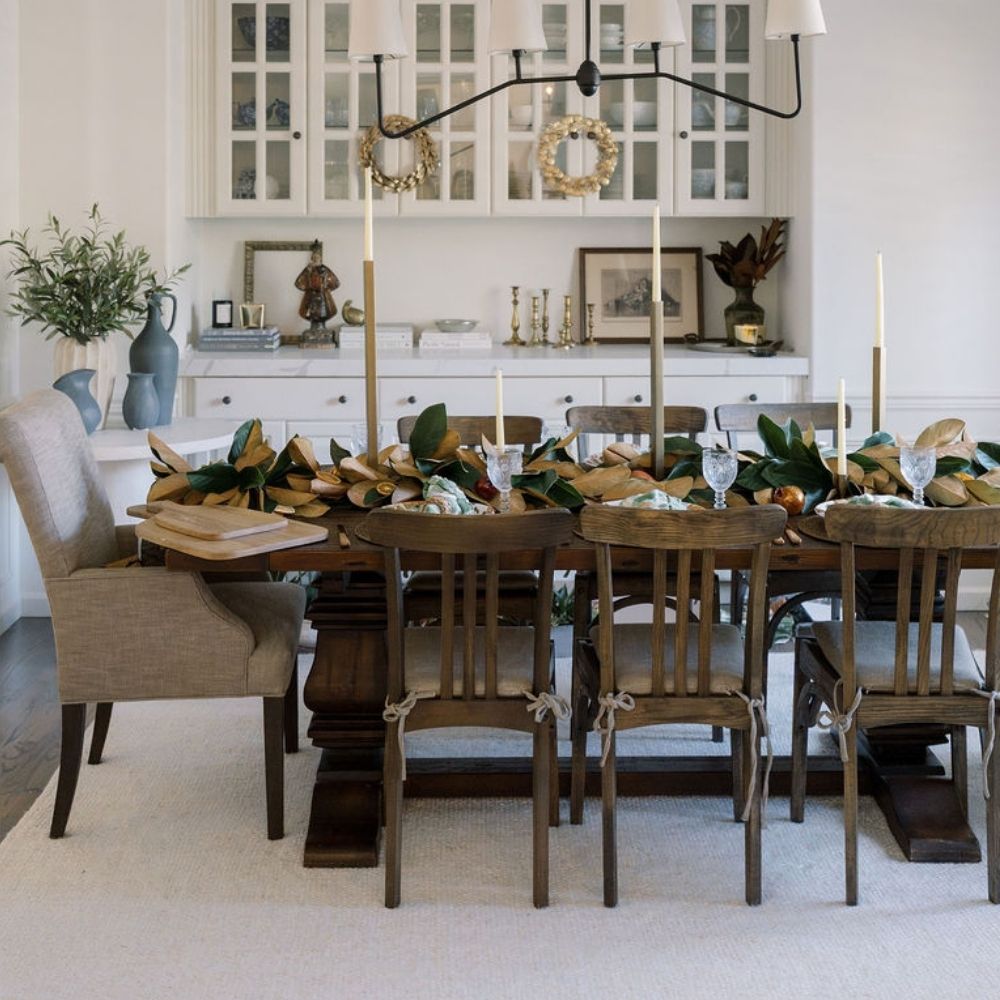 Dining room featuring gold-finish iron taper candle holders on a wooden table with greenery and place settings