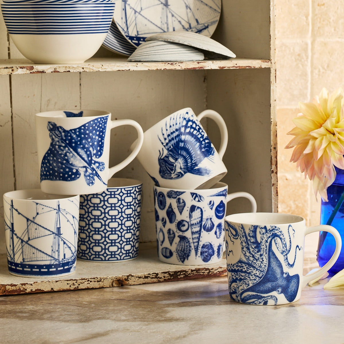 	Spiky Fish Mug displayed with assorted blue-and-white coastal mugs on a rustic kitchen shelf