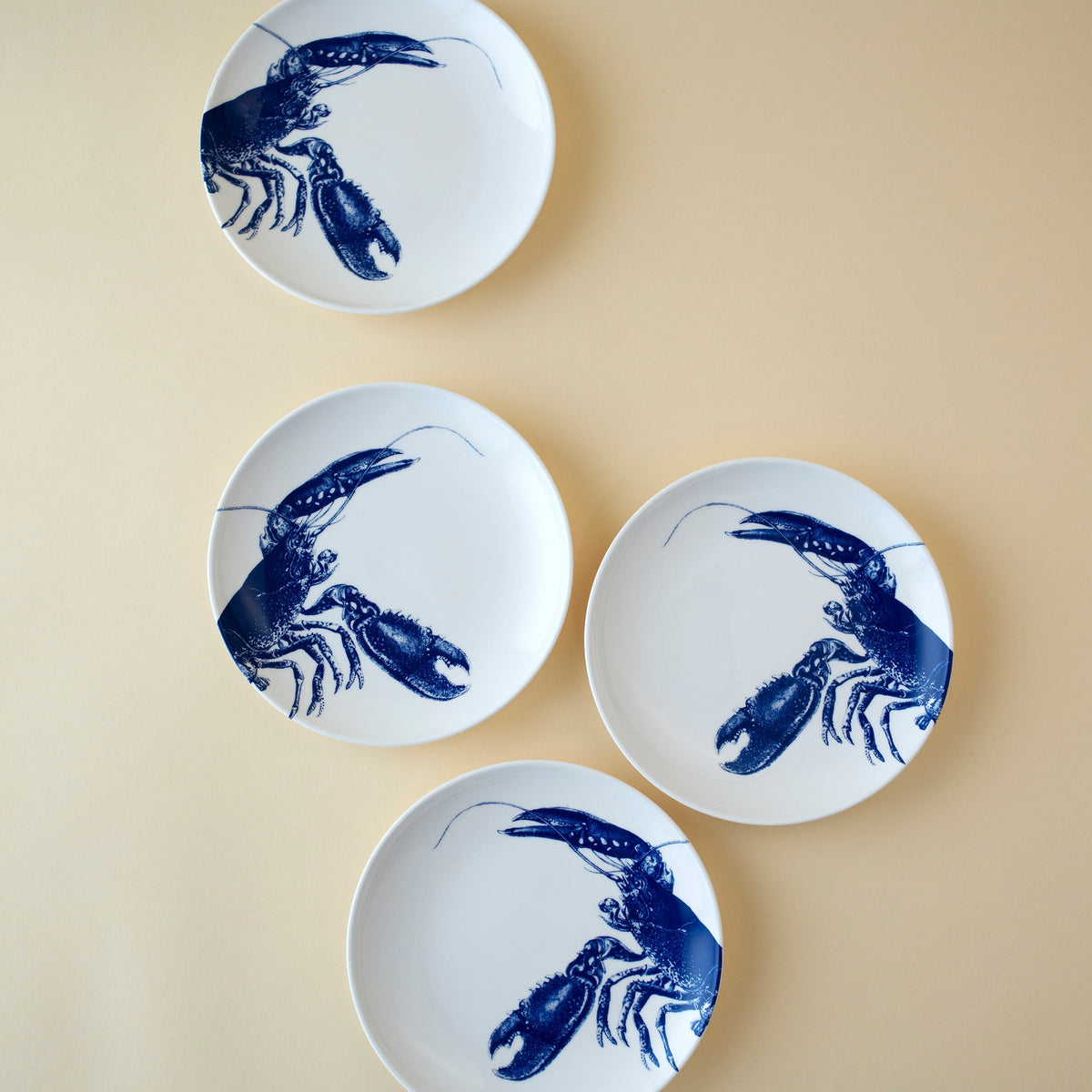 	Four blue lobster porcelain appetizer plates arranged on a pale yellow background
