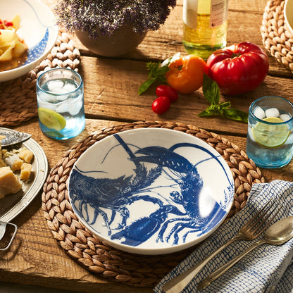 	Blue lobster porcelain bowl on a woven placemat at a wooden dining table with blue glasses and vegetables