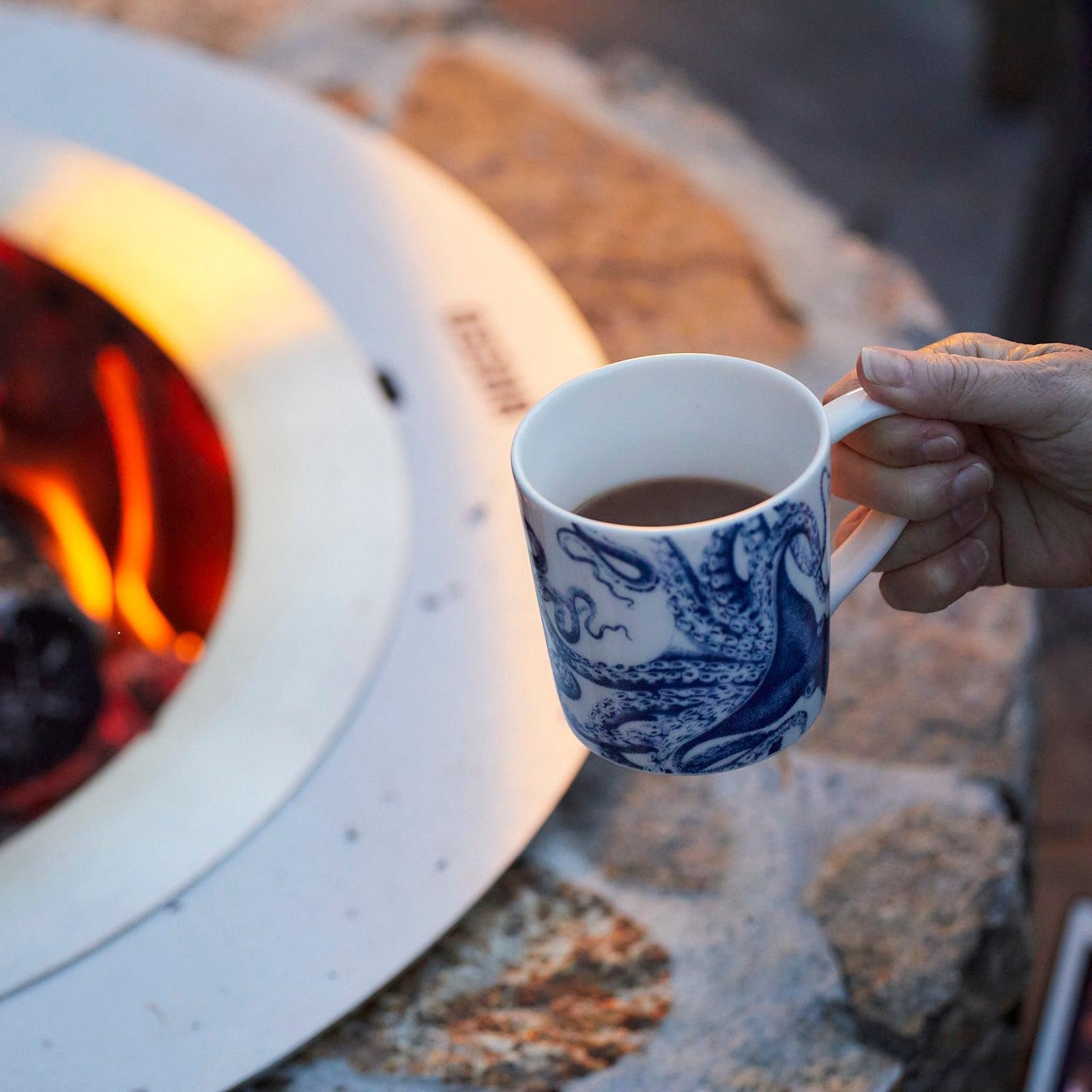 a person holding a cup of coffee in front of a fire