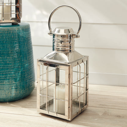 Metal lantern with a clear glass panel, holding a candle, next to a decorative blue vase.