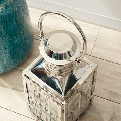 Silver lantern with a handle, resting on wooden flooring beside a blue textured vase.