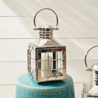 Metal lantern with a glass enclosure and white candle, placed on a textured teal surface.