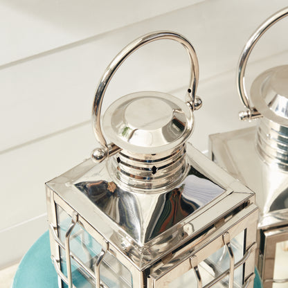 Silver lanterns with glass panels and round handles, resting on a turquoise surface.