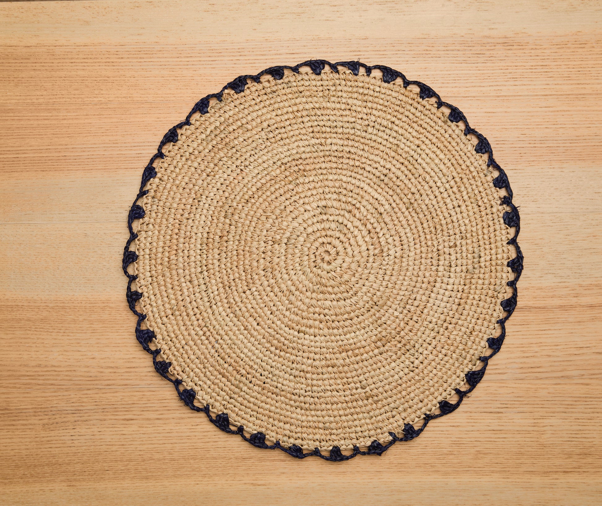 Round woven placemat with black trim on a wooden surface