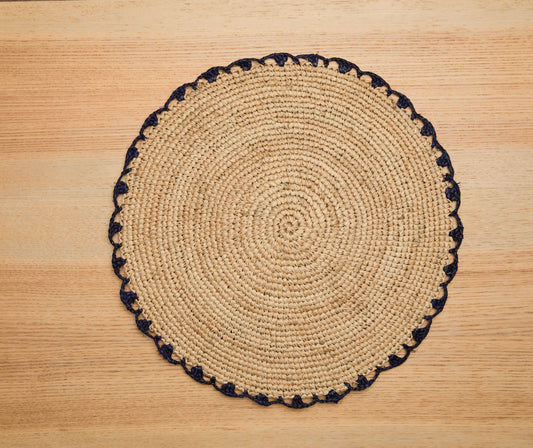 Round woven placemat with black trim on a wooden surface
