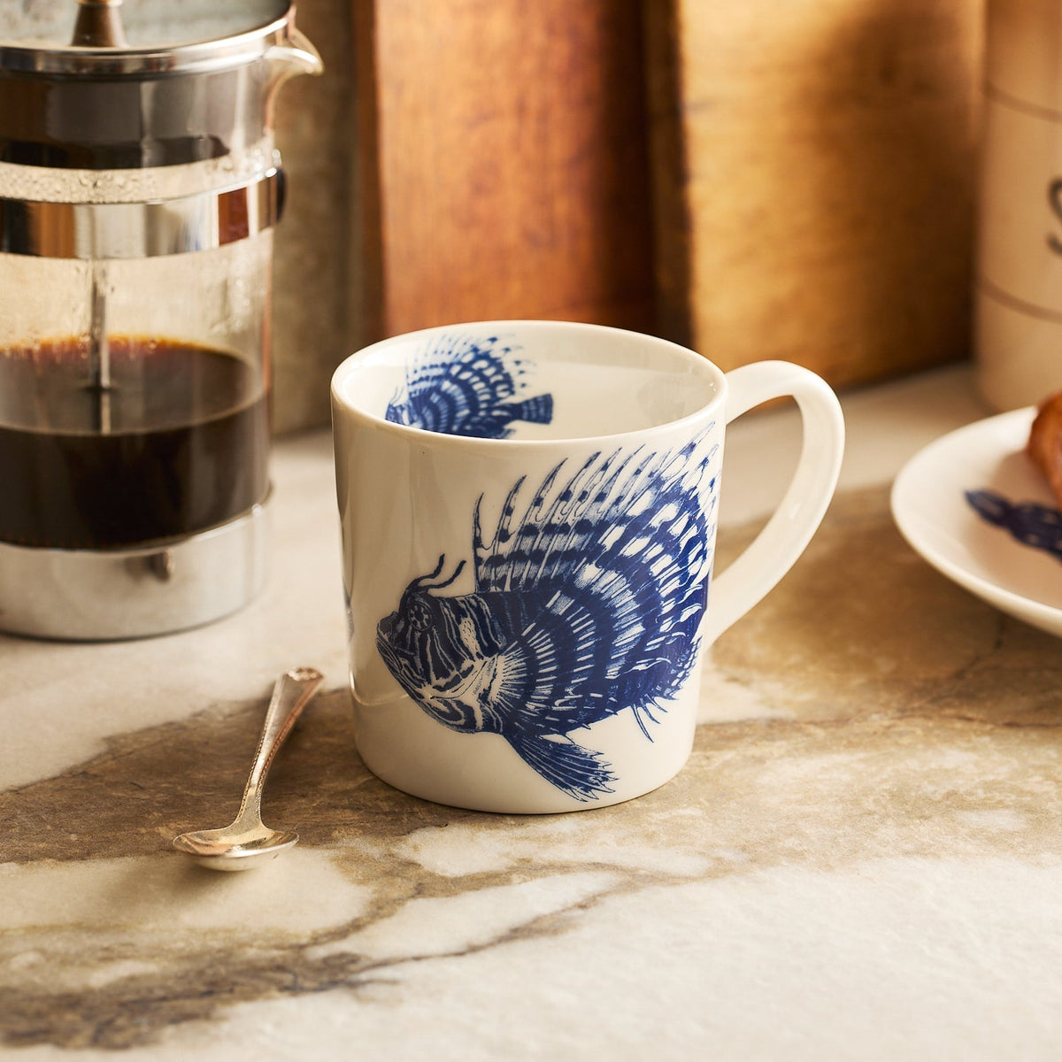 	Blue Spiky Fish Mug beside a French press and spoon on a kitchen counter