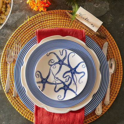 	Blue starfish small plate layered with striped and scalloped dinnerware over a red napkin and woven charger