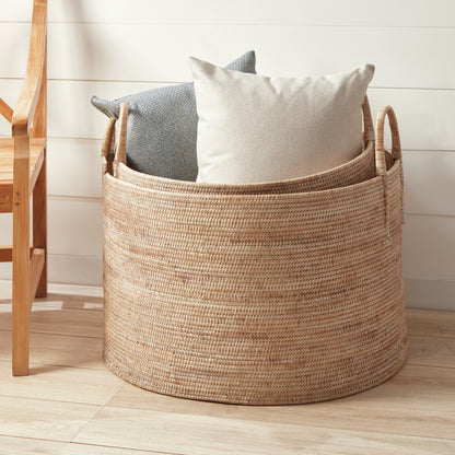 Woven basket holding two decorative pillows, with a wooden chair nearby.