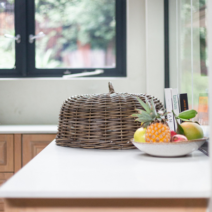 Rattan dome food cover styled on a kitchen island beside a bowl of fruit