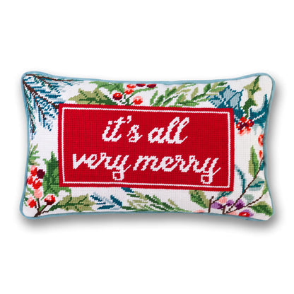 It’s All Very Merry needlepoint pillow with white lettering on red, a festive botanical border, and light blue piping