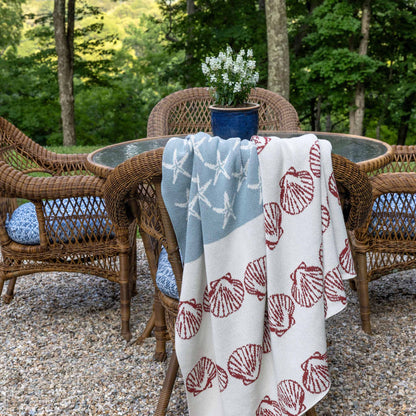 	Coastal Flag starfish and seashell blanket draped over a woven chair beside an outdoor dining table