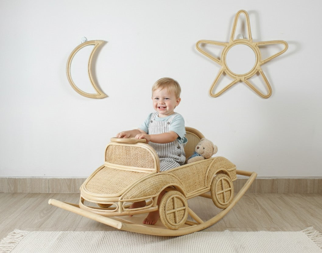 Child seated in a natural rattan rocking car beneath moon and star wall mirrors