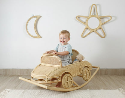 Child seated in a natural rattan rocking car beneath moon and star wall mirrors