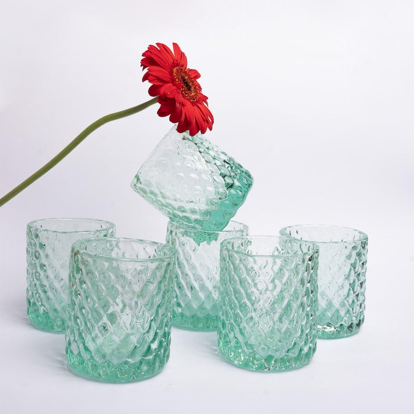 a red flower is in a green glass vase