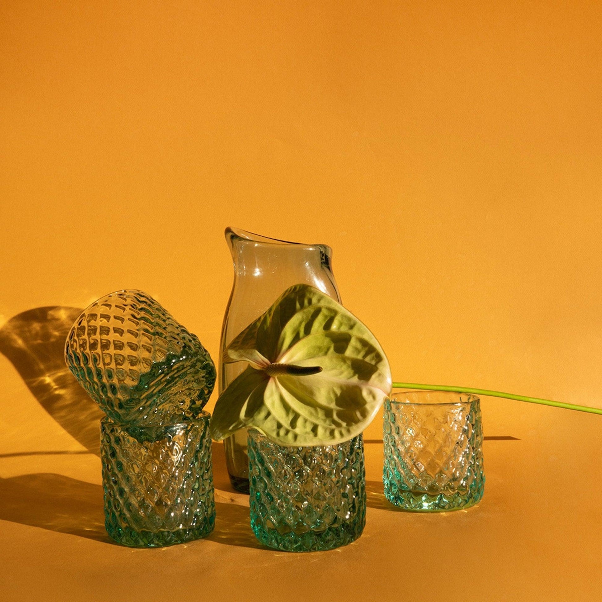 a glass vase with a flower in it next to two glasses